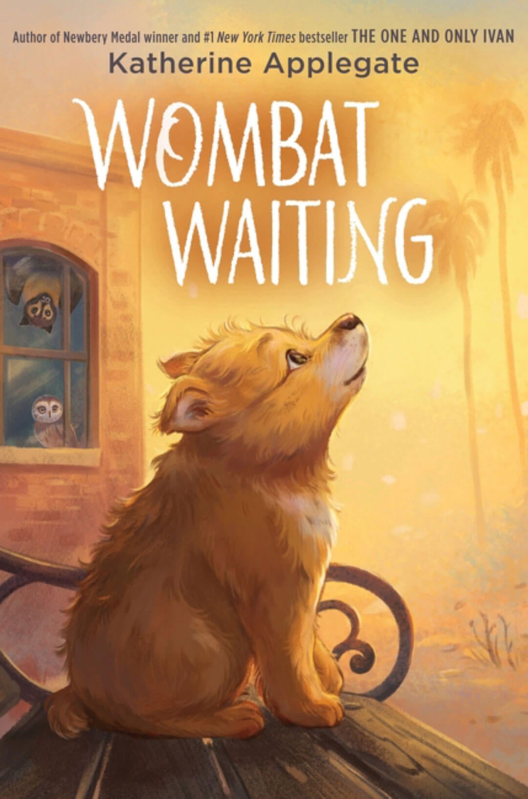 Wombat Waiting by Katherine Applegate. A fluffy, orange-brown baby wombat sits on a curved park bench, looking up toward a golden sunset. At an adjacent brick building window, an owl and another animal are visible.